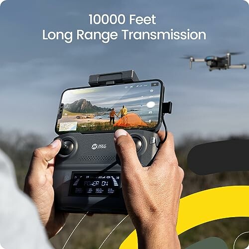 Drone controller with smartphone display and drone flying in the background.